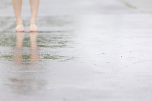 雨が降りはじめる水たまりを歩く足元の靴と反射