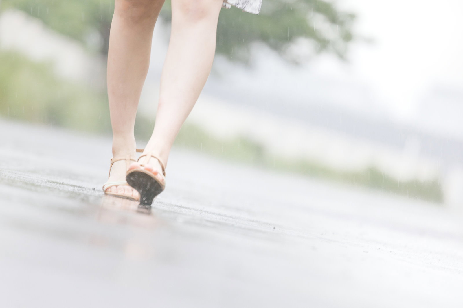 雨の降る濡れた路面をサンダルで歩く女性の足元を後方から捉えた一枚［モデル：佐竹PP］