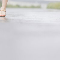 雨で濡れた道を歩く女性の足元のの写真