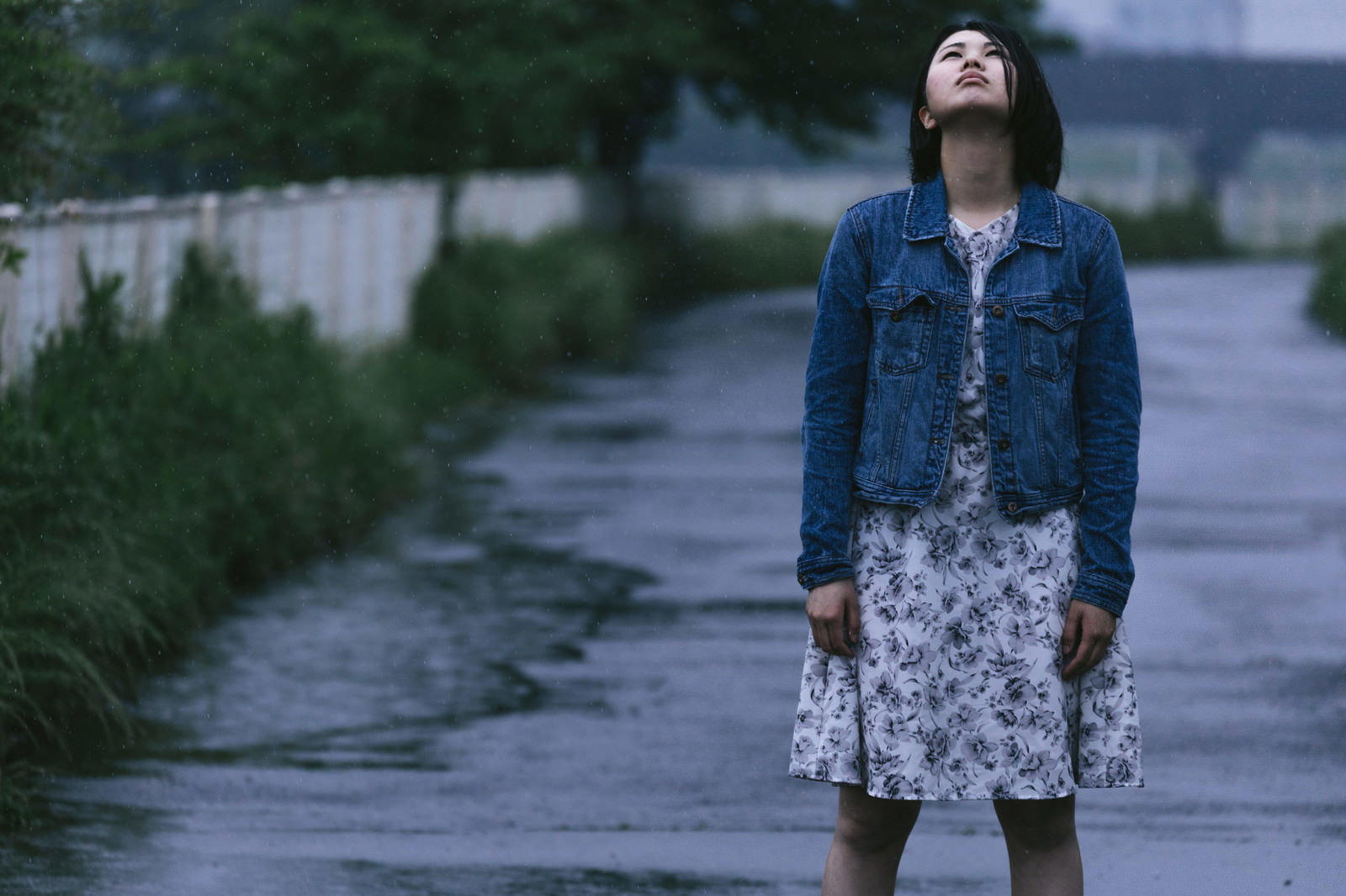 雨に濡れながら空を見上げるデニムジャケット姿の女性［モデル：佐竹PP］