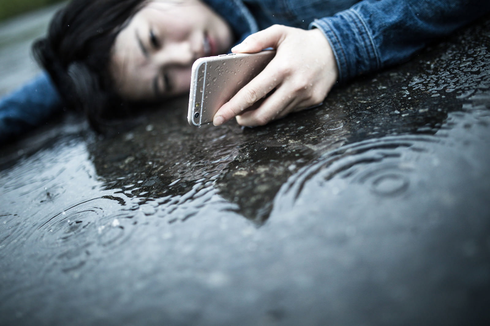 雨に濡れた路面に座り込むデニムジャケット姿の女性［モデル：佐竹PP］