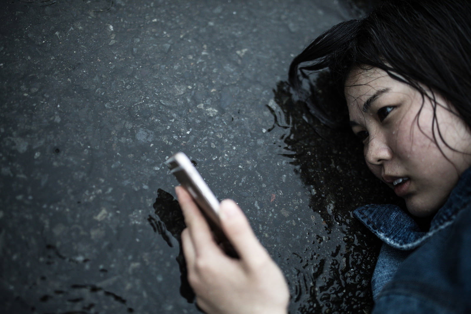 雨の中で地面に座り込みスマートフォンを見つめる悲しそうな女性［モデル：佐竹PP］