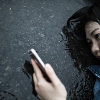 いかにも悲しい雨のシーンでスマホを見つめる女性の写真