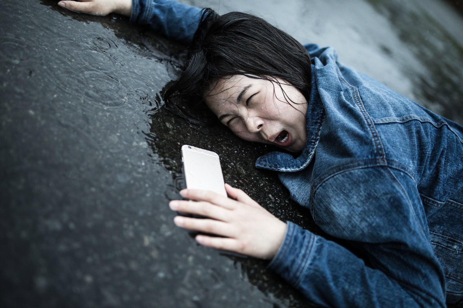 雨の日に水たまりで転倒してスマートフォンを握りしめる女性［モデル：佐竹PP］