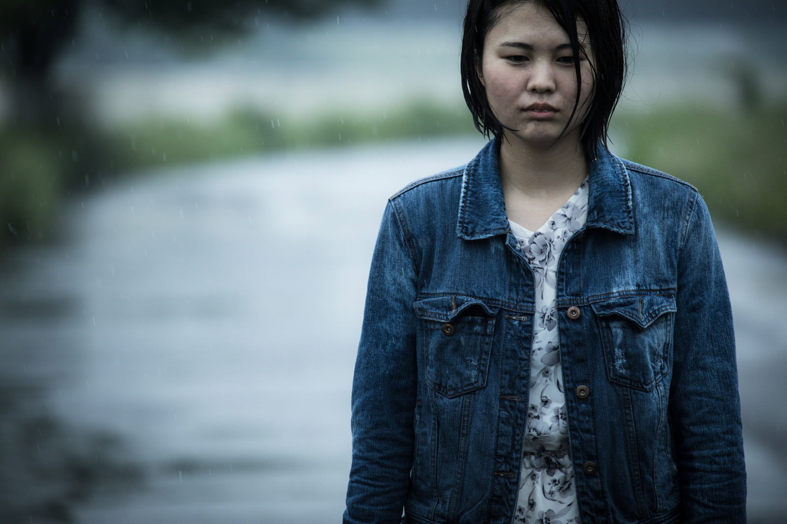 雨に濡れたデニムジャケットを着た女性が曇り空の下に立っている［モデル：佐竹PP］