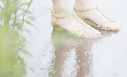 薄いピンクの靴で水たまりを歩む女性の足元