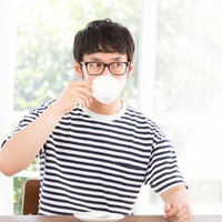 リビングの窓際で深煎りコーヒーを飲む眼鏡の男性の写真