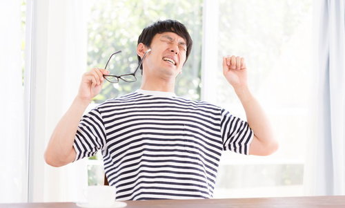 作業の合間に伸びをする男性、眼鏡を手に持ちあくびをする