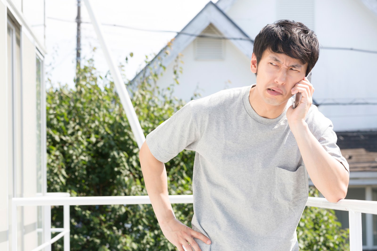 自宅の庭先でスマートフォンを使い通話する、厳しい表情の男性。こめかみに手を当て激怒している［モデル：大川竜弥］