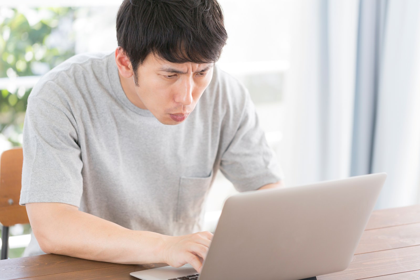 ノートパソコンを前に眉をひそめて困っている男性［モデル：大川竜弥］