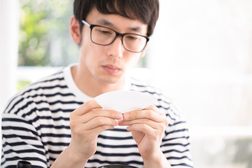 ドリップコーヒーのペーパーフィルターを丁寧に折る眼鏡をかけた男性