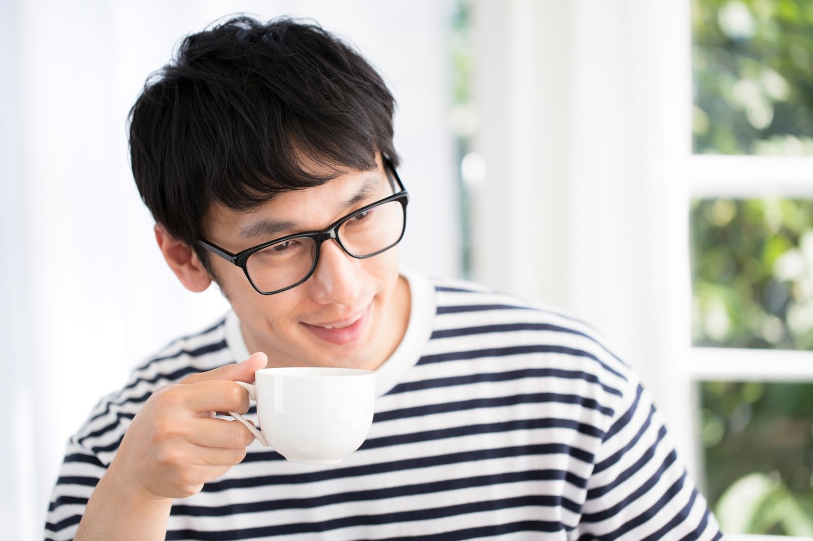 眼鏡の男性がコーヒーを飲みながら笑顔でいる［モデル：大川竜弥］
