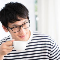 打ち合わせ中にコーヒーを飲みながら笑顔の眼鏡男子の写真