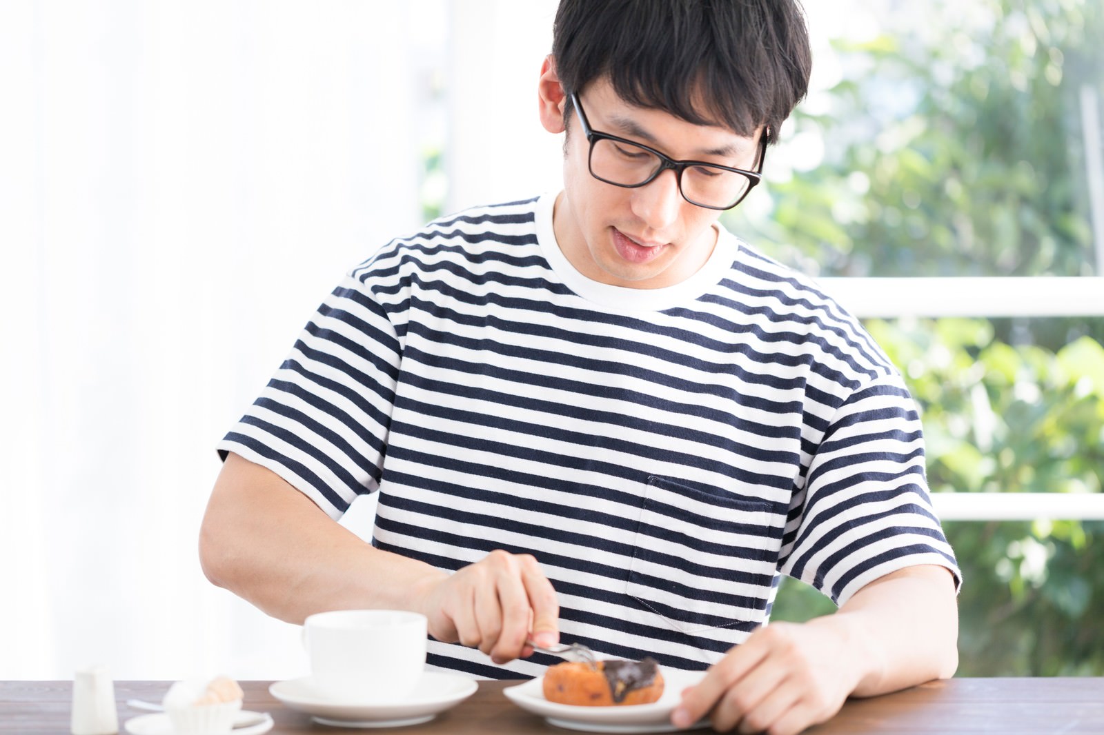 眼鏡の男性がドーナッツをナイフで切りコーヒーで休憩［モデル：大川竜弥］