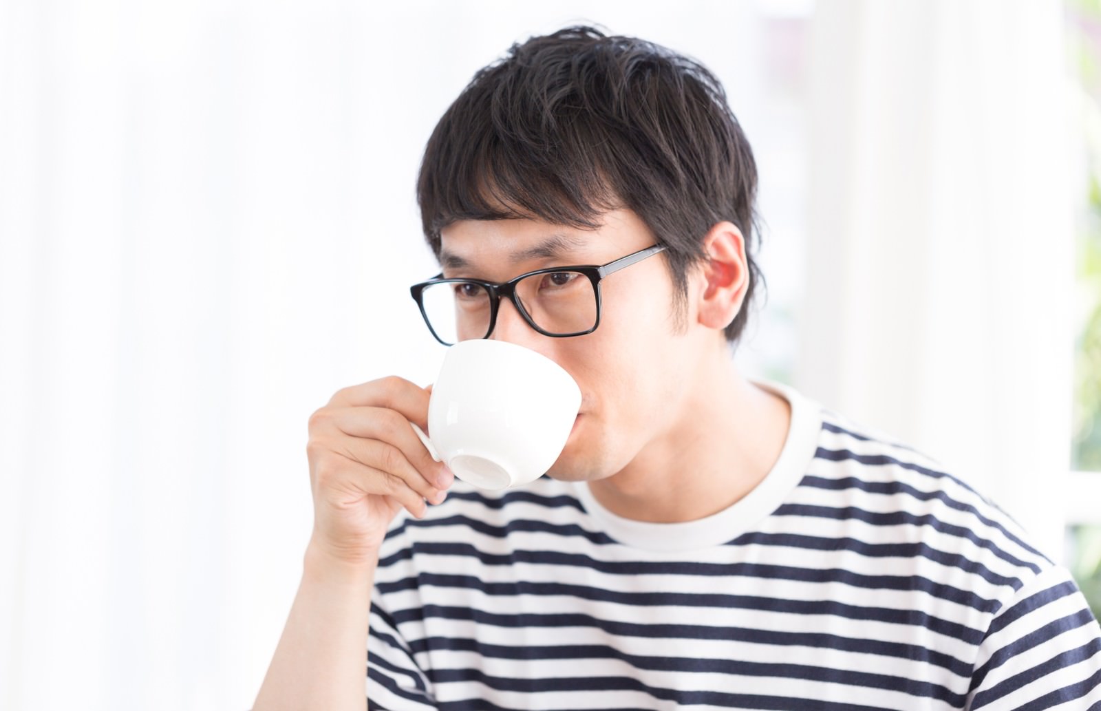 眼鏡の男性が白いカップでコーヒーを飲む［モデル：大川竜弥］