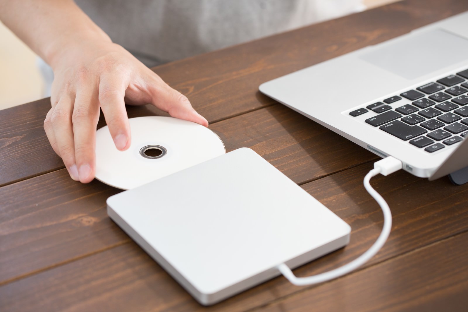 Hands removing a disc from an external DVD drive connected to a laptop