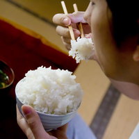 箸で白米を口に運ぶ茶碗のご飯を食べる様子の写真