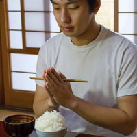箸を手にした和室でご飯とみそ汁を食べる男性の写真