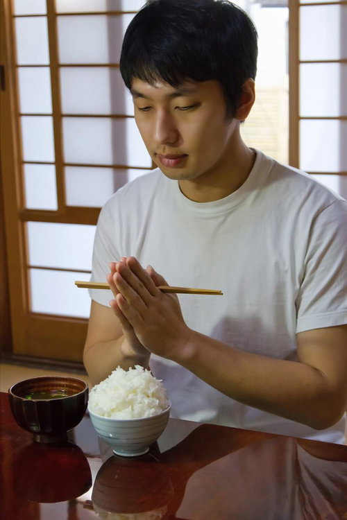 箸を手にした和室でご飯とみそ汁を食べる男性