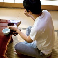 畳の和室で一人でご飯を食べる男性の後ろ姿の写真