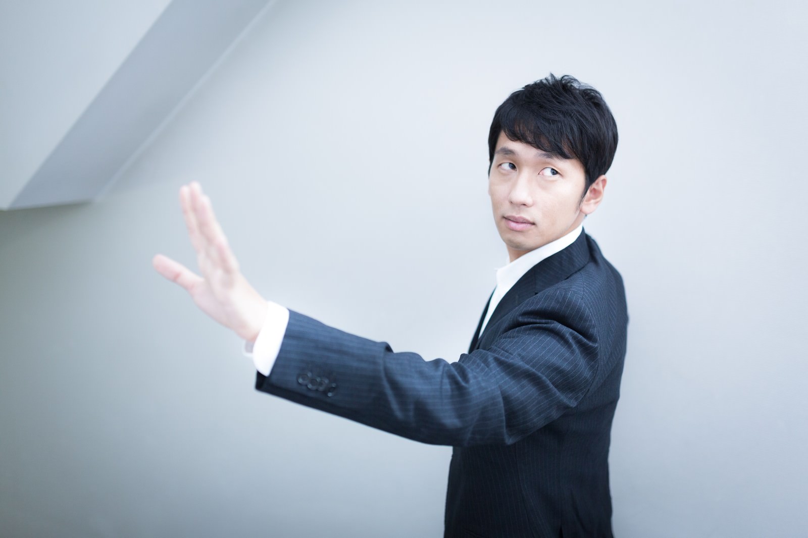 紺色の縦縞スーツを着た男性が、左手を上げて手のひらを開き薬指を見せながら横を向いている［モデル：大川竜弥］