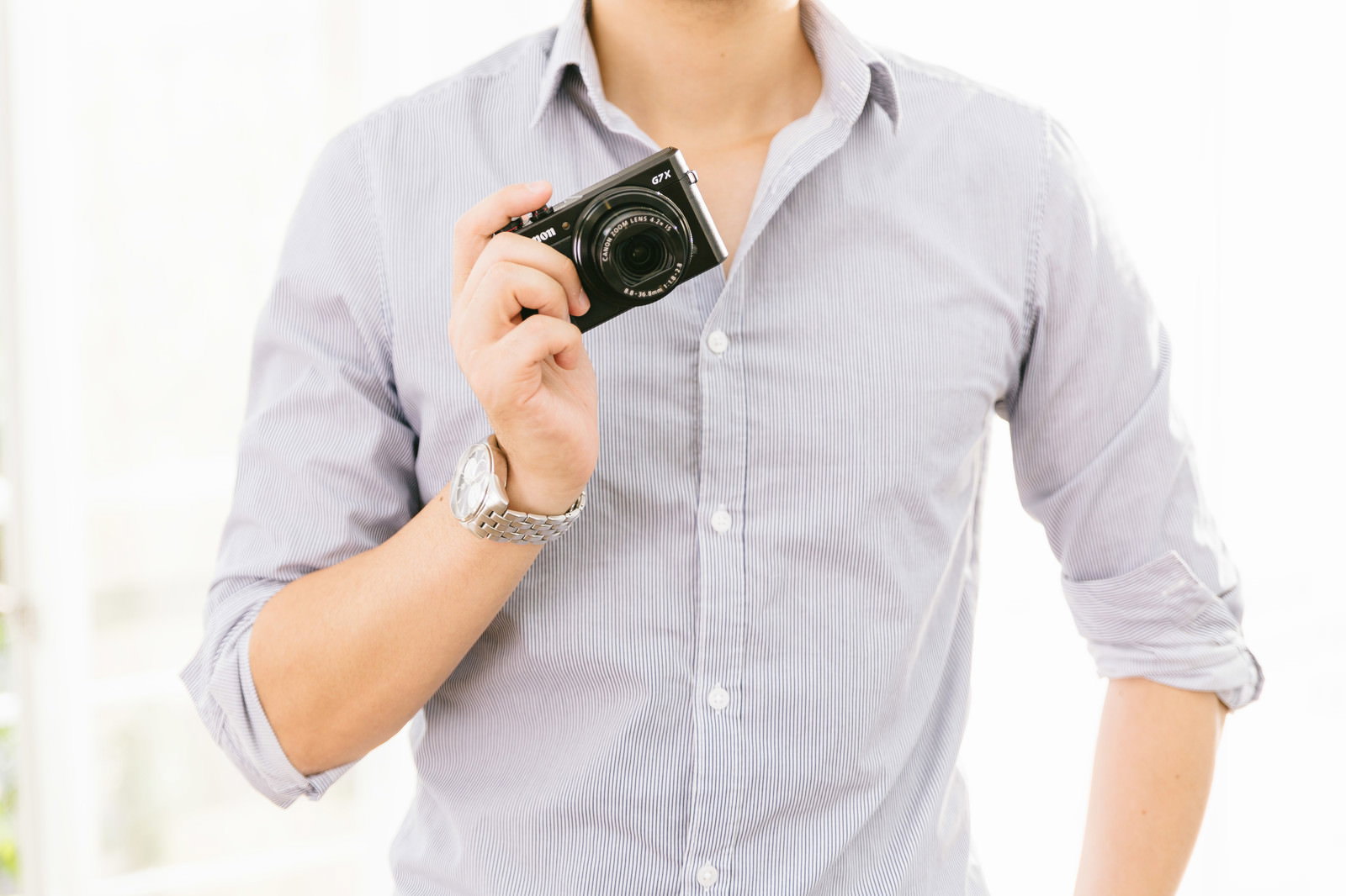 薄紫のシャツを着た男性がコンパクトデジタルカメラを構える