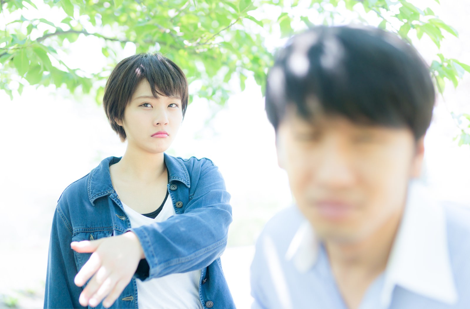デート中に彼氏にビンタをしようとする女性と、緑の木をバックに向かい合うカップル［モデル：モデルヒロ 大川竜弥］