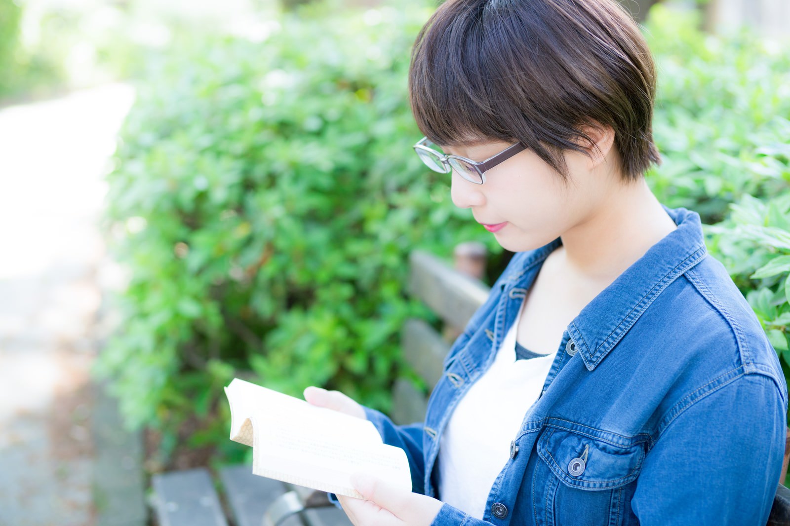 公園のベンチで本を読む眼鏡をかけた女性［モデル：モデルヒロ］