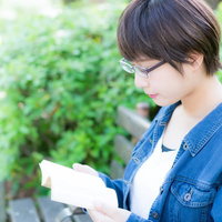 公園のベンチで読書をする眼鏡をかけた文学少女の写真