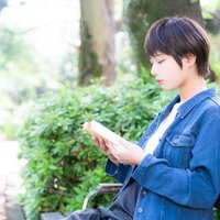 ベンチでラノベを読みながら彼氏を待つ健気な女性の写真