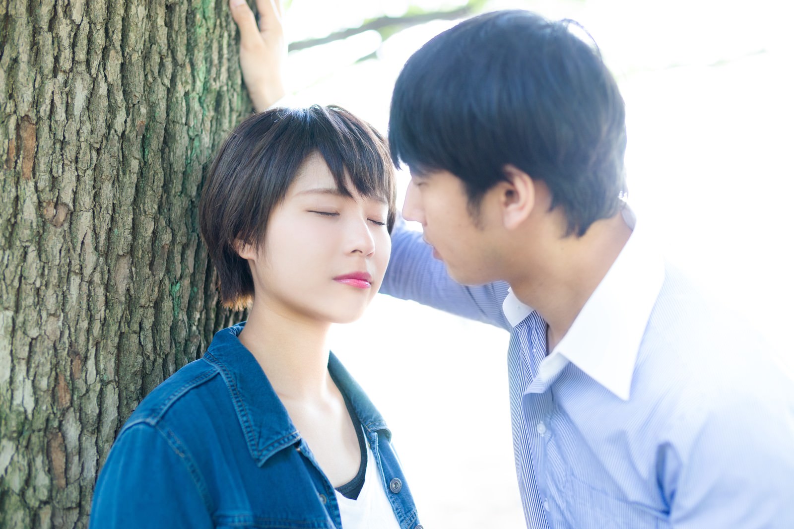 樹木の前でキスしようとするカップルの男性と女性の写真［モデル：モデルヒロ 大川竜弥］