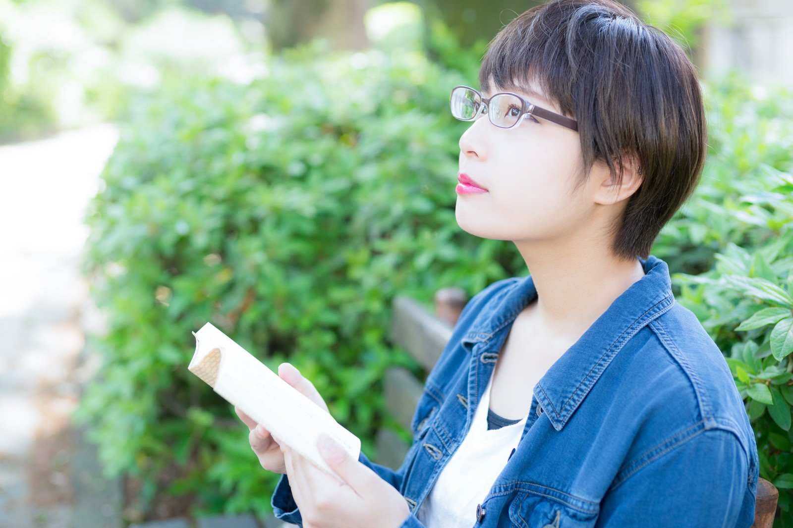 公園のベンチで本を読むメガネをかけた女性［モデル：モデルヒロ］