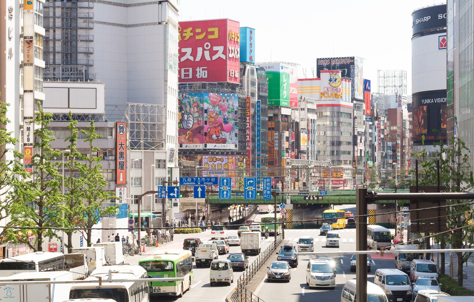 新宿駅東口の繁華街の大通りで走る車と立ち並ぶ看板
