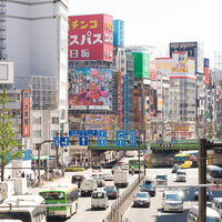 新宿駅東口の大通りを行き交う車と看板、高層ビルの写真