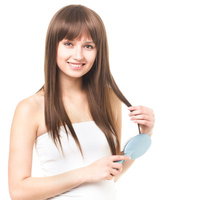 水色のヘアブラシで髪をとかす笑顔の白いチューブトップの女性の写真