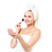 化粧ブラシとピンクのコンパクトを持つ頭にタオルを巻いた笑顔の女性の写真