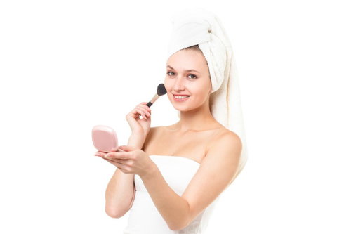 化粧ブラシとピンクのコンパクトを持つ頭にタオルを巻いた笑顔の女性