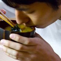 茶碗を両手で持ってお味噌汁をすする男性の写真