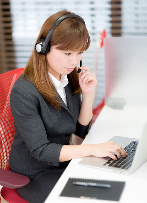 ヘッドセットでパソコン操作するスーツの女性