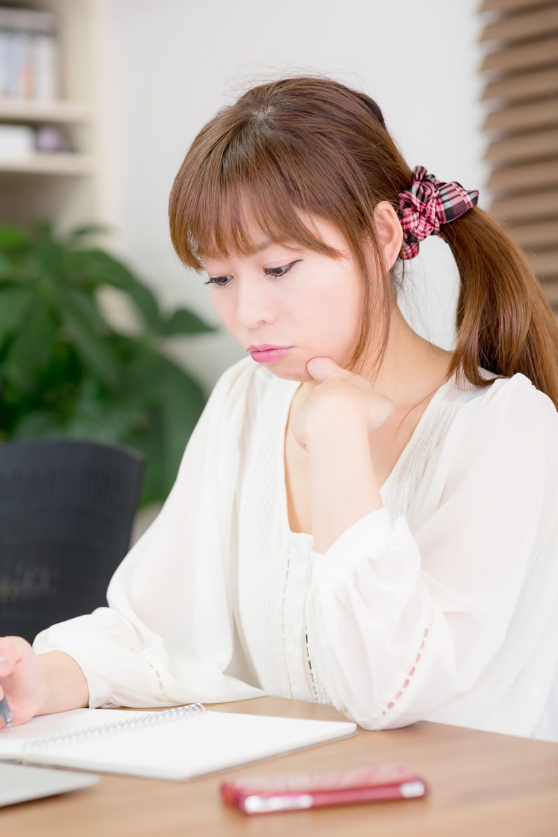 ピンクのシュシュをつけてノートを見ながら勉強する女性［モデル：暢子］