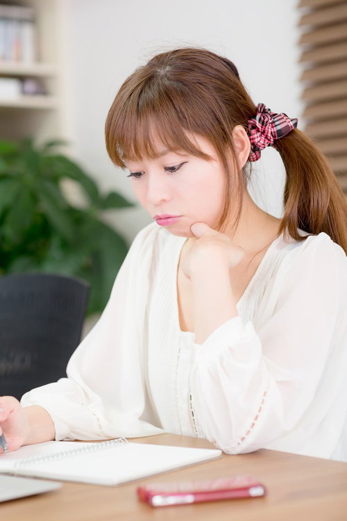 ノートを見ながら顎に手を当てて考えるポニーテールの女性