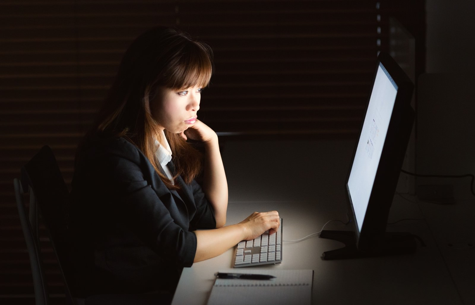 消灯した室内でモニターの光に照らされながらパソコン作業をする女性［モデル：暢子］