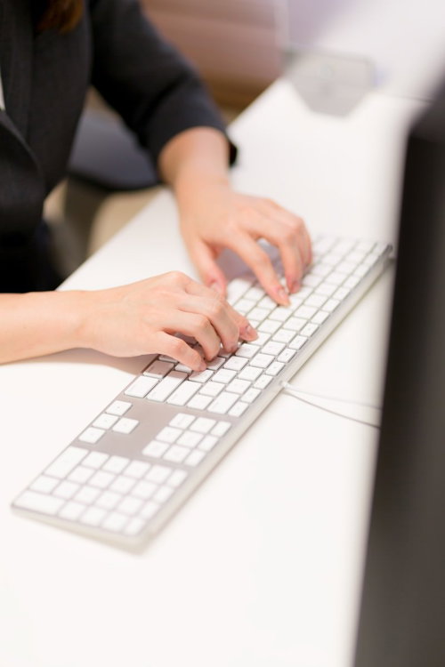 白いキーボードをタイピングする女性の手元