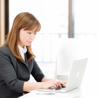 オフィスの窓際でノートパソコンを操作する女性の写真