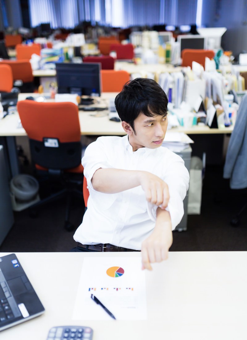 オフィスで両袖をまくった白いワイシャツを着た男性が自信に満ちた表情でカメラを見ている［モデル：大川竜弥］