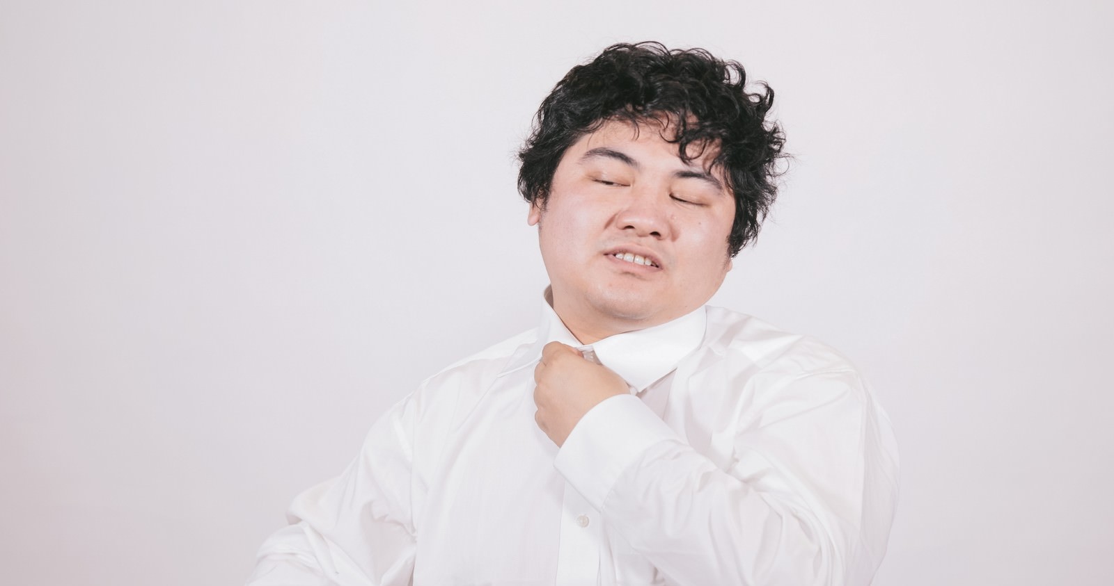 白いワイシャツを着て困った表情を浮かべる太った男性［モデル：段田隼人］