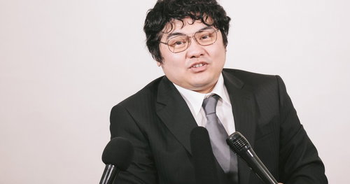 マイクを前に話す記者会見の広報男性、スーツ姿で企業発表