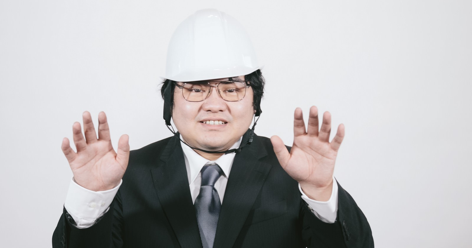 白いヘルメットを着用した男性が両手を上げて制止のポーズをとっている［モデル：段田隼人］