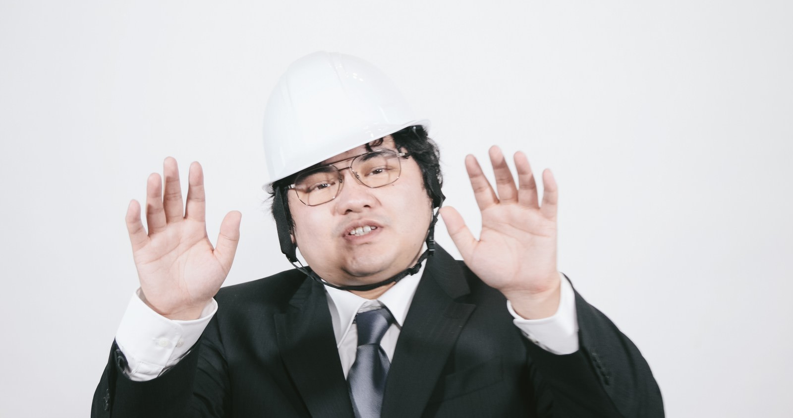 ヘルメットを被り緑のスーツを着た男性職員が両手を前に出して制止のポーズをとっている［モデル：段田隼人］