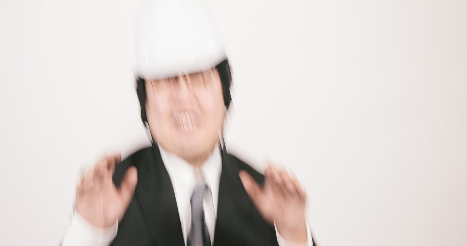 白いヘルメットを被り両手を前に出して制止ポーズを取るスーツ姿の男性［モデル：段田隼人］